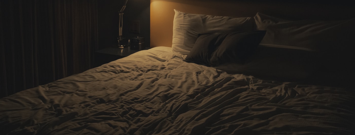 A bedside table lamp switched on next to a bed